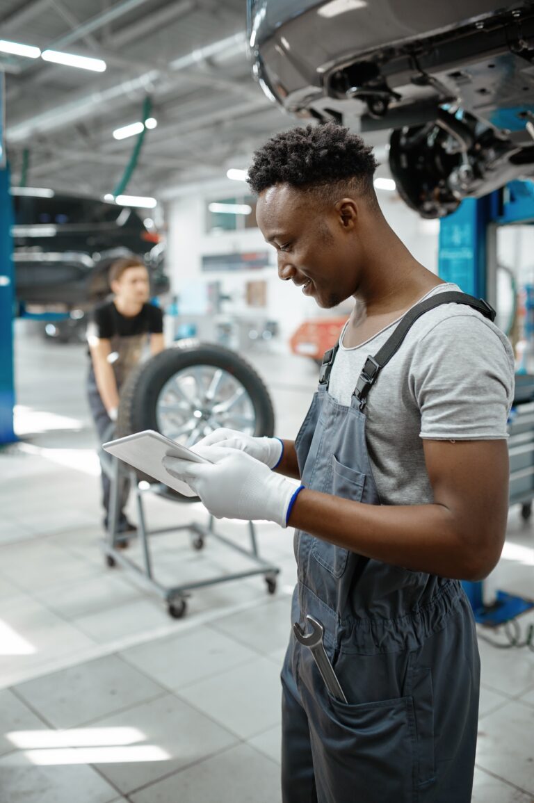 Mechanic using laptop, car on lift, auto service